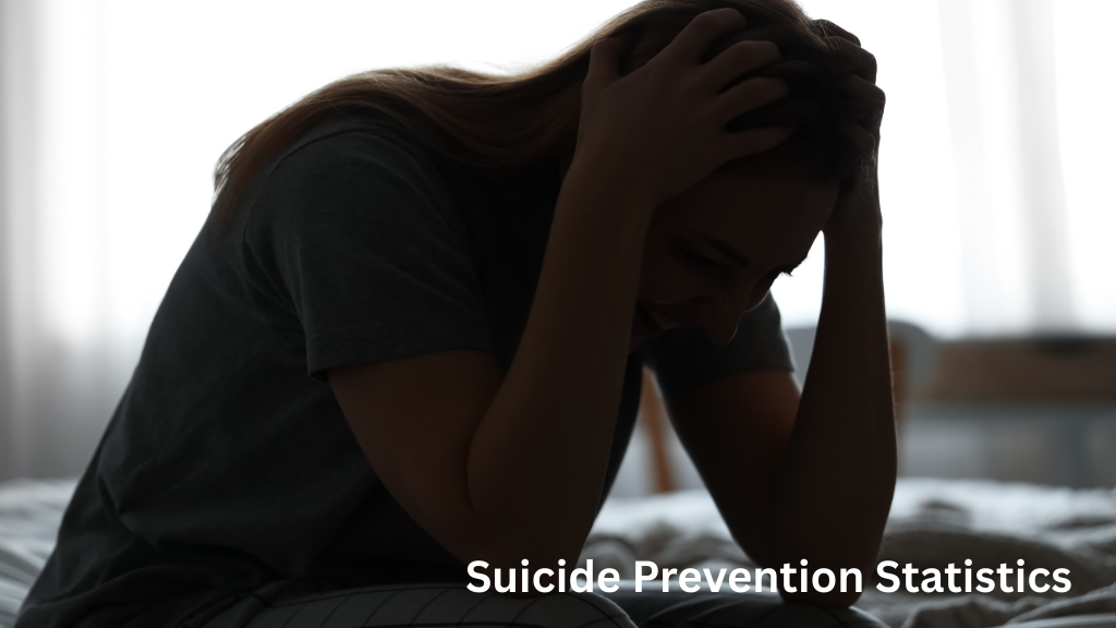 Person sitting on a bed holding their head in distress, illustrating suicide prevention statistics and mental health struggles.