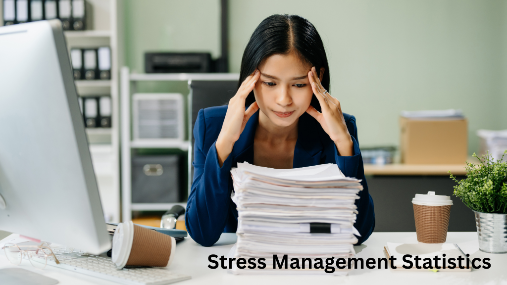 Woman sitting at a desk with a large stack of paperwork and holding her head, illustrating stress management statistics and workplace stress.